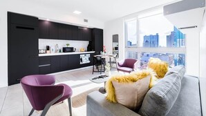 A modern kitchen with black cabinets, a white countertop, and a city view through large windows. - Skyline View Condo with Pool (Miami)
