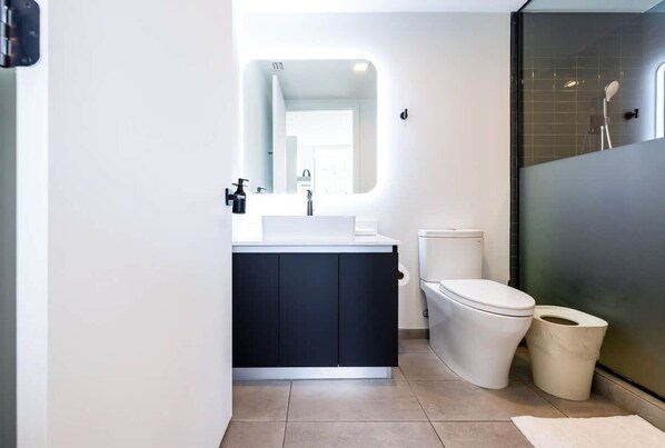 A modern bathroom with a white sink, dark cabinets, a white toilet, and a glass shower enclosure.