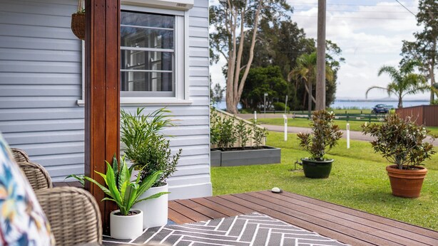 A wooden deck with potted plants, a white chair, and a view of the garden and street. - Long Jetty Lake House -Long Jetty, Central Coast Fully Renovated 3 bed Cottage,  (Long Jetty)