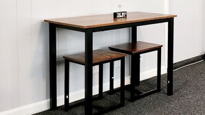 Une pièce avec un mur recouvert de panneaux blancs, une table en bois sur laquelle est posée une pancarte, et des œuvres d’art encadrées.