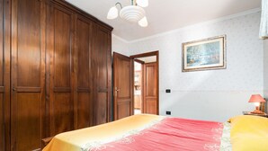 Een slaapkamer met een bed, een houten garderobe en een schilderij aan de muur.