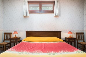 Une chambre à coucher avec un lit, deux tables de chevet, deux chaises, une fenêtre avec des rideaux et un papier peint à motifs floraux.