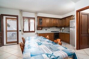 Un coin repas avec une table dressée pour quatre personnes, des meubles en bois, un réfrigérateur et une porte-fenêtre coulissante donnant sur un espace extérieur.
