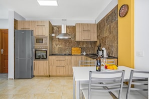 A modern kitchen with a refrigerator, oven, microwave, and wooden cabinets. - Vacation Apartment 'La Octava Isla' with Shared Pool, Wi-Fi (Puertito de Güimar)