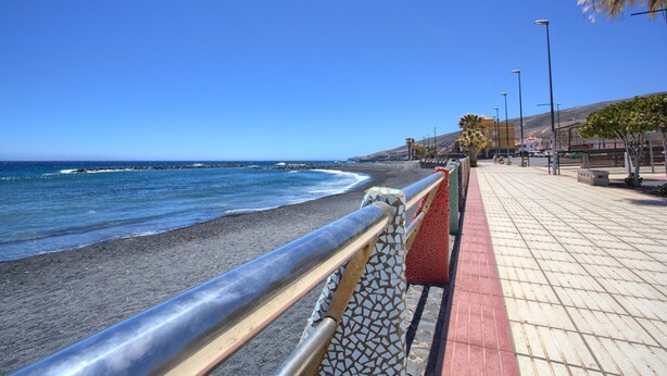 A coastal walkway with a metal railing, a tiled path, and a clear view of the ocean.