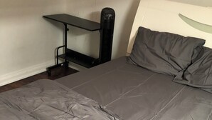 Una cama con edredón gris, una mesita de noche negra y una pared blanca.
