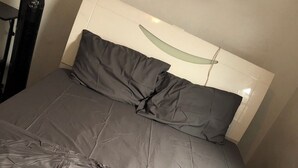 Una cama con cabecera blanca y ropa de cama gris.
