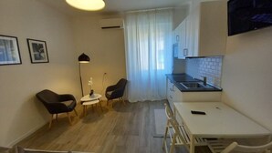A compact living space with a kitchenette, a dining area with two chairs, a small table, and a TV mounted on the wall. - Hostmate- Milano - Piazza Insubria (Milano)