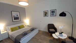 A modern bedroom with a bed, bedside tables, a chair, a small table with a plant, and framed pictures on the wall. - Hostmate- Milano - Piazza Insubria (Milano)
