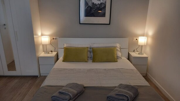 A neatly made bed with two pillows, two bedside lamps, and a framed picture on the wall. - Hostmate- Milano - Piazza Insubria (Milano)