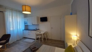 A compact room with a kitchenette, a dining area, a bed, and a TV mounted on the wall. - Hostmate- Milano - Piazza Insubria (Milano)