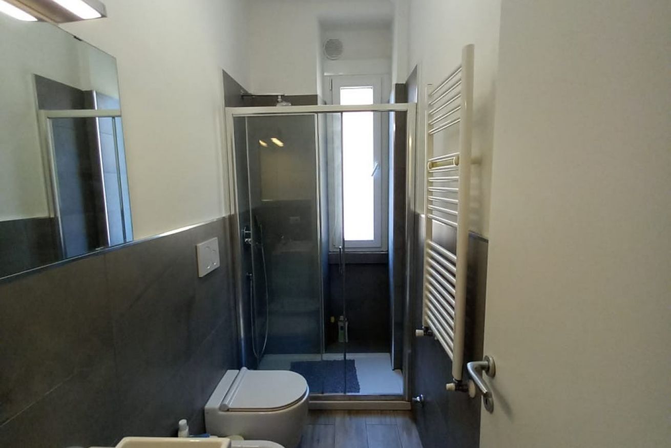 A narrow bathroom with a toilet, a glass-enclosed shower, and a towel rack.