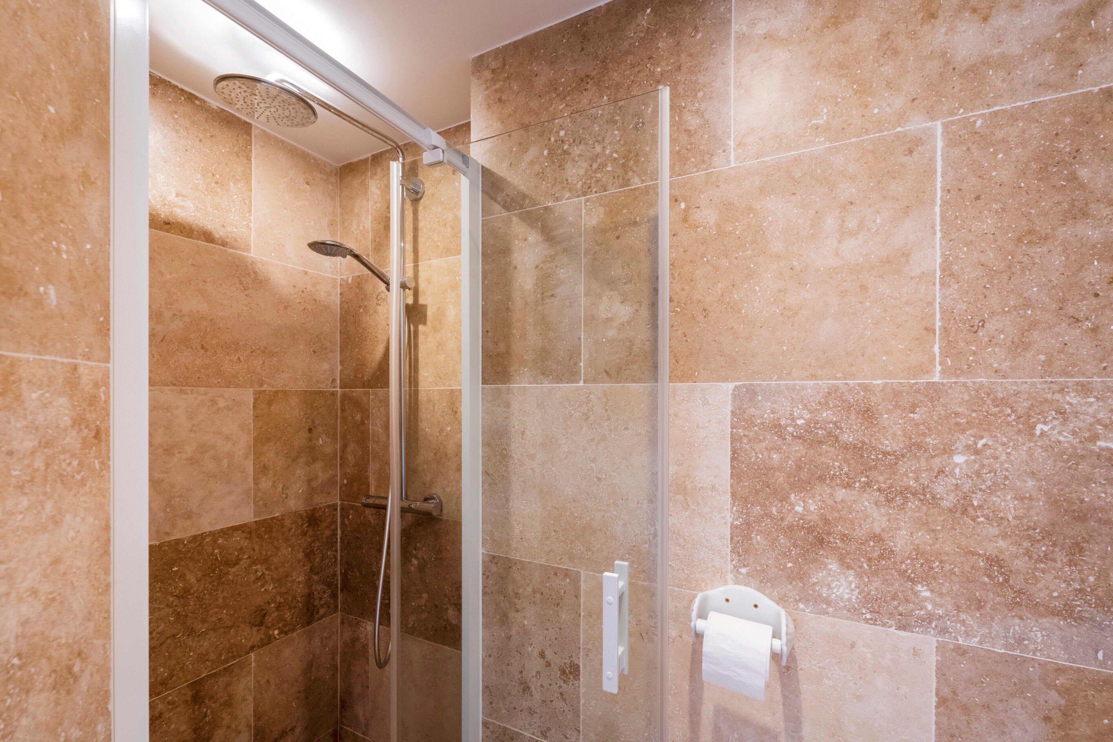 Eine Dusche mit Glastür, Handbrause und Handtuchhalter.