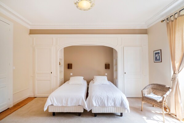Une chambre avec deux lits, une chaise en osier et une porte blanche.
