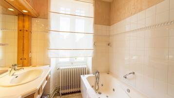 Un bagno con lavandino, vasca e finestra con persiane.