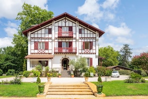 A two-story building with a symmetrical facade, a central entrance with steps, and a driveway leading to a parked car.