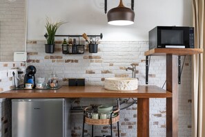 A kitchen with a brick wall, a wooden countertop, a sink, a microwave, and a coffee machine.
