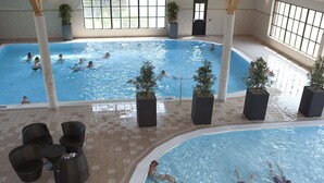 Una piscina interior con múltiples carriles, rodeada de plantas en macetas y mobiliario de mimbre.