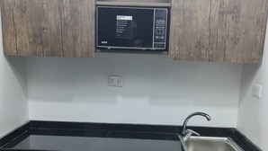 A compact kitchen with wooden cabinets, a black countertop, a stainless steel sink, and a refrigerator. - Royal House (Irbid)