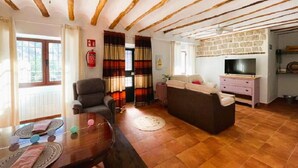 A cozy living room with a wooden ceiling, a sofa, a TV, and a dining table with placemats.