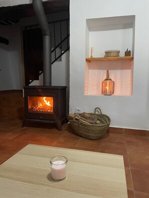 Habitació amb una llar de llenya, una cistella de vimet, una espelma i una estant amb un fanal.