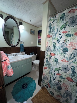 Un baño con lavamanos, inodoro y espejo. Hay una cortina de ducha con estampado de peces.