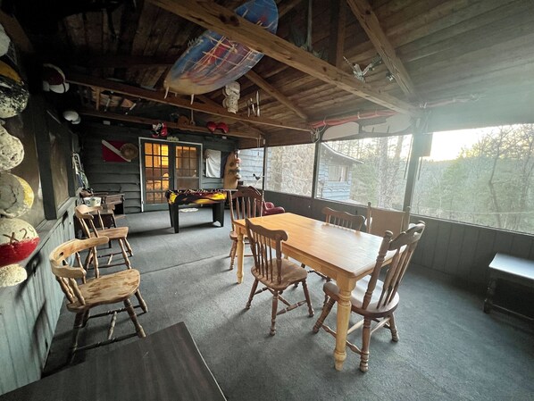 Un interior rústico de madera con una mesa y sillas para comer, un banco y una decoración con una tabla de surf.