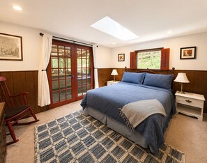 A bedroom with a bed, a nightstand, a chair, a window with shutters, and a skylight. - Charming & Historical 3-bedroom cabin in marvelous Franklin with AC, fast WiFi (Franklin)