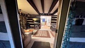 A cozy living room with a sofa, coffee table, and a rug. There is a stone wall and a wooden ceiling. - Charming & Historical 3-bedroom cabin in marvelous Franklin with AC, fast WiFi (Franklin)