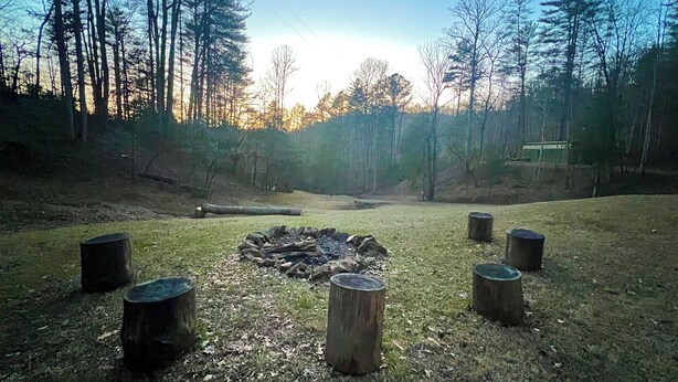 A forest clearing with a central fire pit surrounded by wooden stumps, surrounded by trees and a clear sky. - Charming & Historical 3-bedroom cabin in marvelous Franklin with AC, fast WiFi (Franklin)