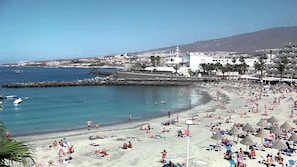 Une scène de plage côtière, avec un ciel dégagé, une plage de sable et une digue rocheuse.