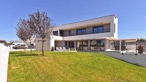 Una casa moderna de dos pisos con techo plano, ventanas amplias y un área de estar exterior cubierta.