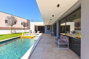 A modern outdoor pool area with a clear blue pool, lounge chairs, and a glass-enclosed patio.