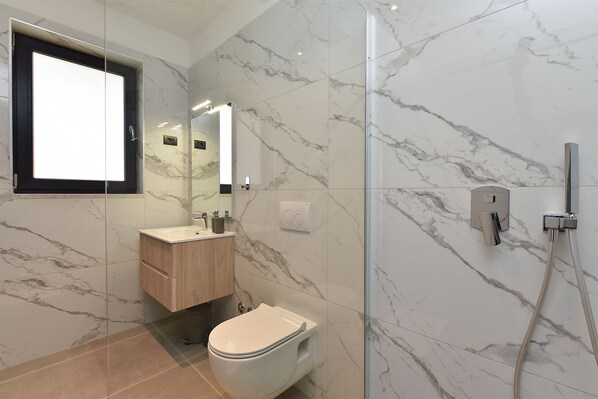A modern bathroom with a glass shower enclosure, a marble-tiled wall, a wooden vanity, and a toilet.