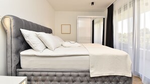 Una cama bien hecha con un cabecero tapizado de color gris, ropa de cama blanca y una manta de color blanco.