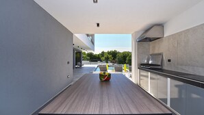 Una cocina moderna con una encimera larga, un bol de fruta y vistas a una piscina y zona de estar al aire libre.