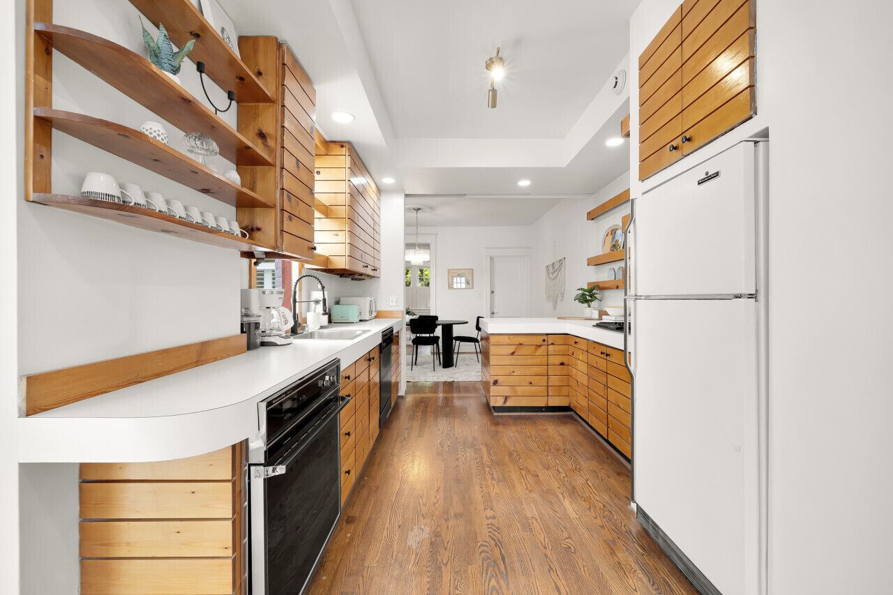 Una cocina moderna con armarios de madera, encimeras blancas y horno empotrado.