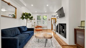A living room with a blue sofa, a round wooden coffee table, and a TV mounted on the wall.