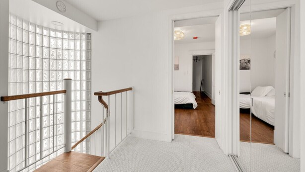 A modern hotel room with a wooden staircase, a large window with frosted glass, and a view into another room.