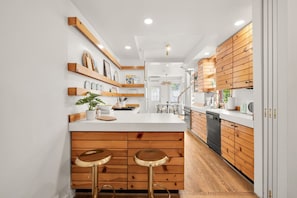 Une cuisine moderne avec des meubles en bois, un plan de travail blanc et deux tabourets.