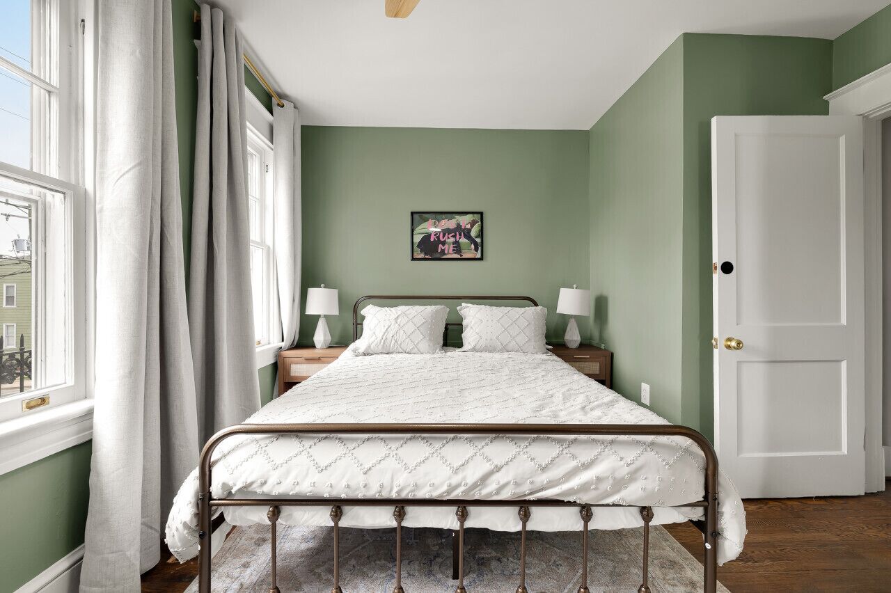 A bedroom with a bed, a nightstand, a lamp, a door, and a window with curtains.