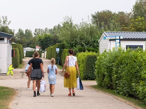 A gravel path with a group of people walking. There are houses on either side, one with a blue sign. - Comfortable Chalet With Microwave, on a Holiday Park 1 km. From the Beach (Koudekerke)