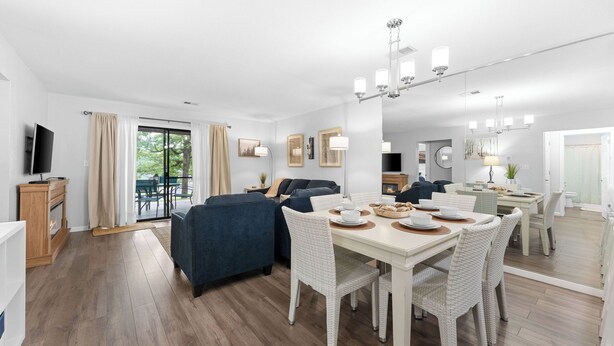 Een moderne woonkamer met een bank, eettafel en stoelen. Er is een televisie, een open haard en een raam met gordijnen.