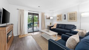 Een moderne woonkamer met een flatscreen televisie, een open haard, een bank, een salontafel en een schuifdeur naar een buitenruimte.