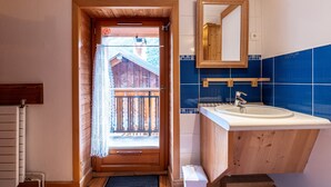 Un baño con puerta de madera que da a un balcón, un lavabo con espejo y paredes de azulejos azules.