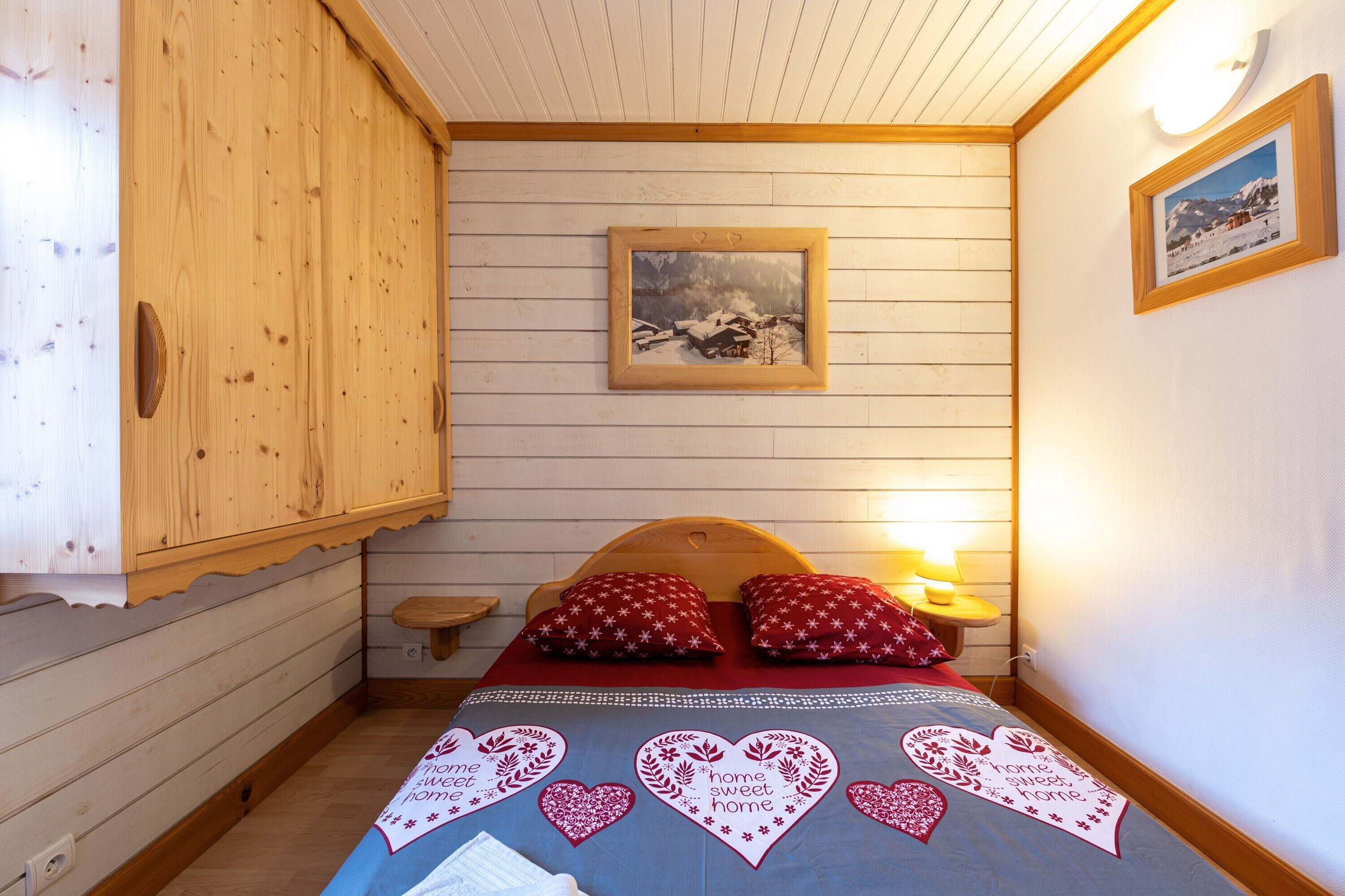 Une chambre avec des murs en bois, un lit avec des oreillers rouges, un tableau encadré au mur et une table de chevet avec une lampe.