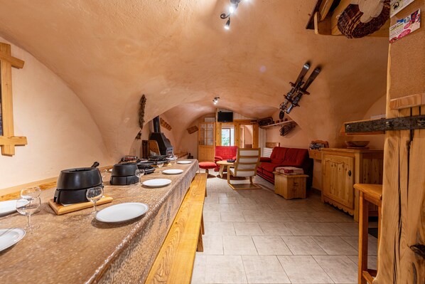 A cozy, rustic kitchen with a long wooden counter, a fireplace, and a dining area with a red sofa.