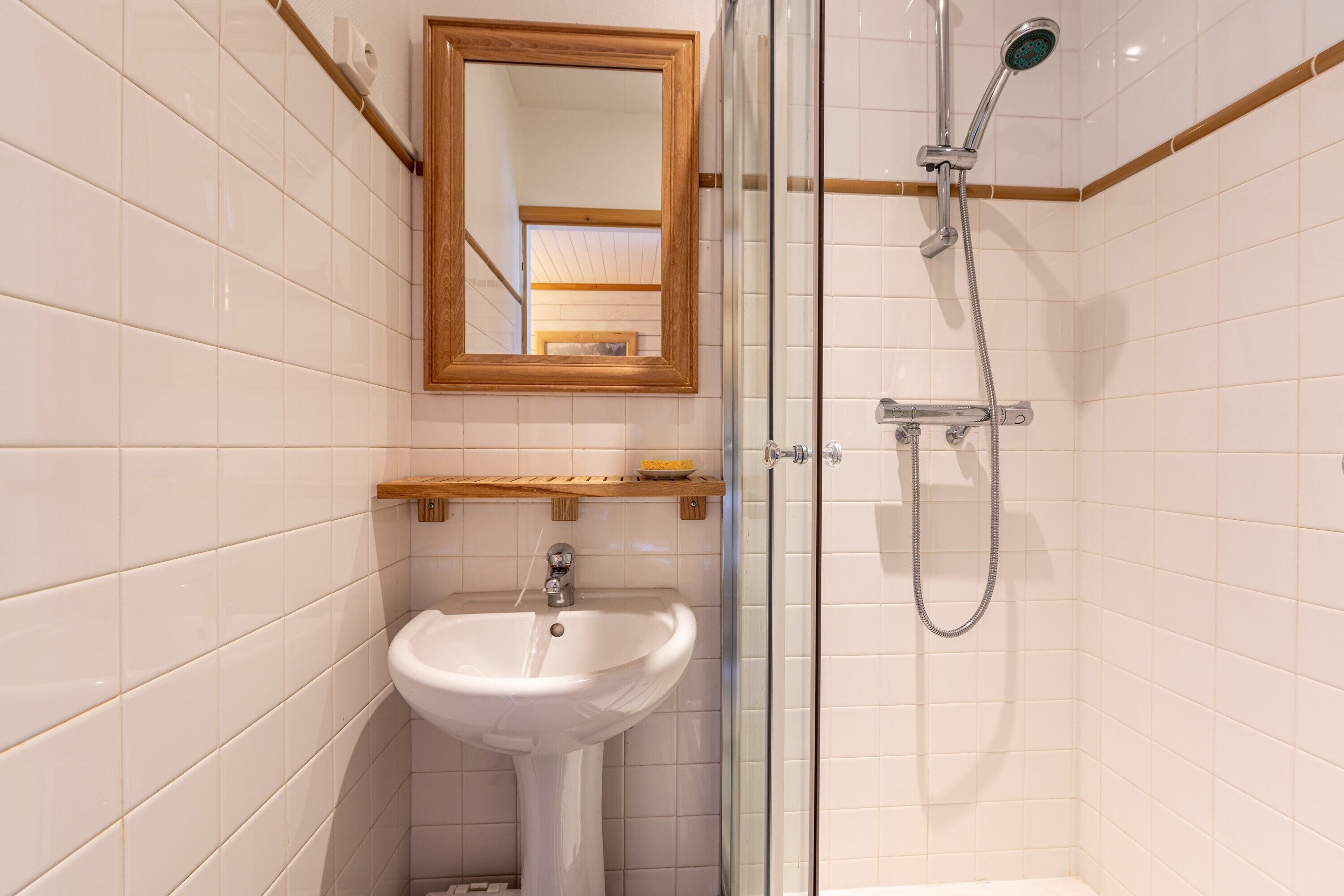 Ein Badezimmer mit einem weißen Waschbecken, einem Spiegel und einer Dusche.