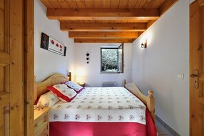 A bedroom with a wooden ceiling, a bed with a red and white quilt, a nightstand, a window, and a wall-mounted picture.