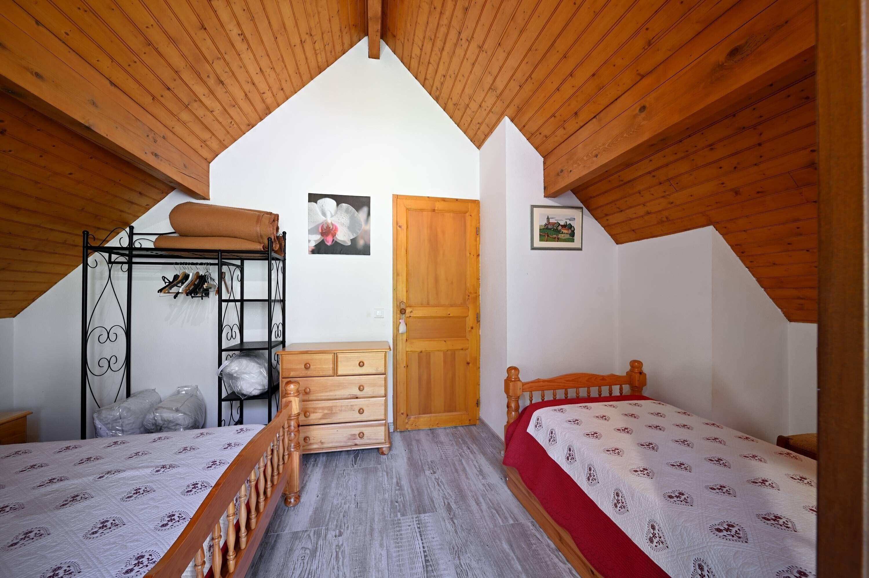 A bedroom with two beds, wooden ceiling beams, a wooden door, and a small shelf with shoes.